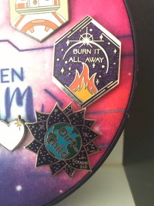 'Dirt Child' on a planet bordered by petals, Aurora Rising enamel pin